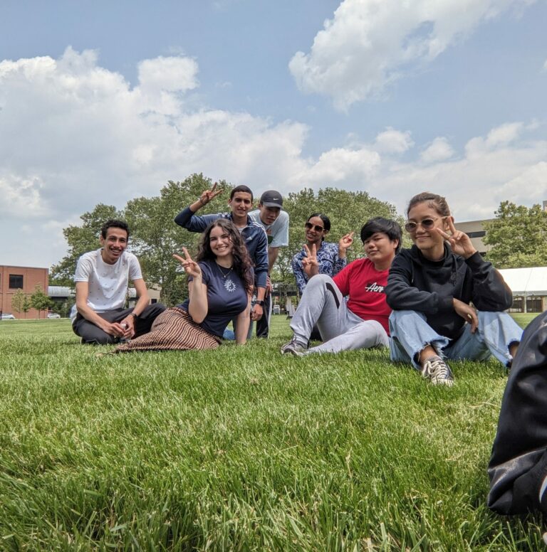 Picture of a group of students sitting in the grass holding up peace signs