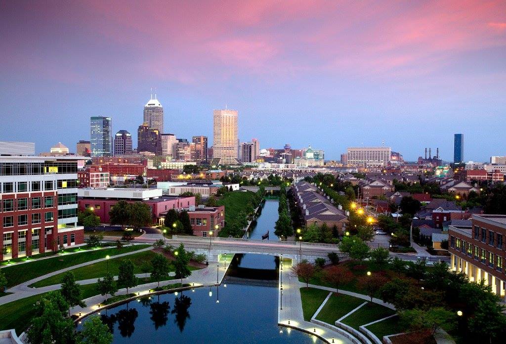 Picture of a city skyline with a light blue sky and pink clouds over the canal in downtown Indianapolis.