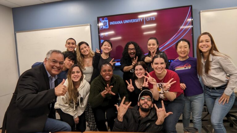 Picture of a group of students with a professor standing in front two white boards and a TV screen in a classroom setting